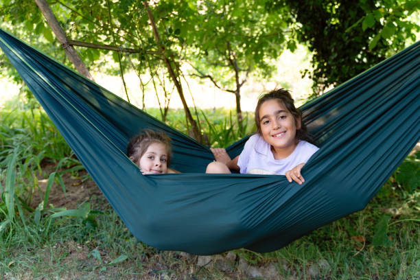 Two little girls sitting side by side in a hammock, smiling and looking at the camera