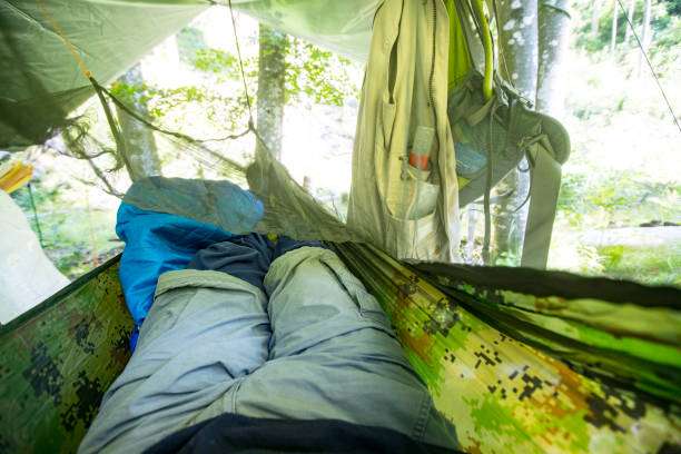 Person relaxing inside a green camping hammock tent with clothes and backpack.