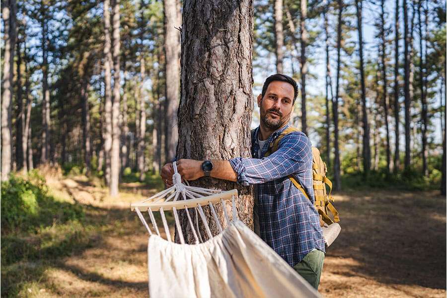 Man with backpack setting up hammock in forest
