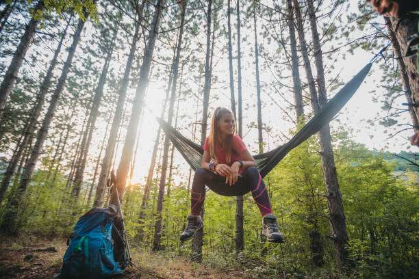 Woman relaxing in a peaceful forest hammock at sunset with a backpack.