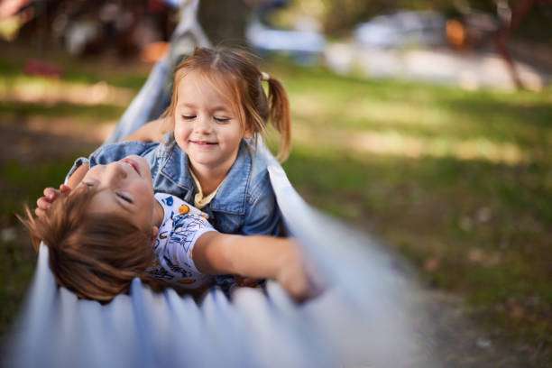 Happy children smiling and relaxing together in a white outdoor hammock.