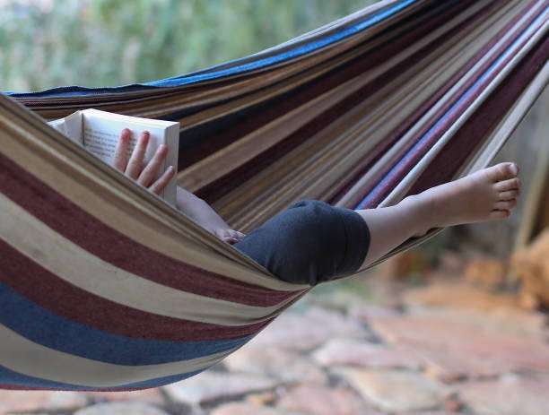 Person relaxing and reading a book comfortably in a striped fabric hammock outdoors.