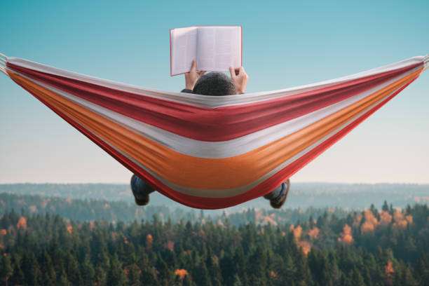Person reading a book in a striped hammock, enjoying a serene forest view.