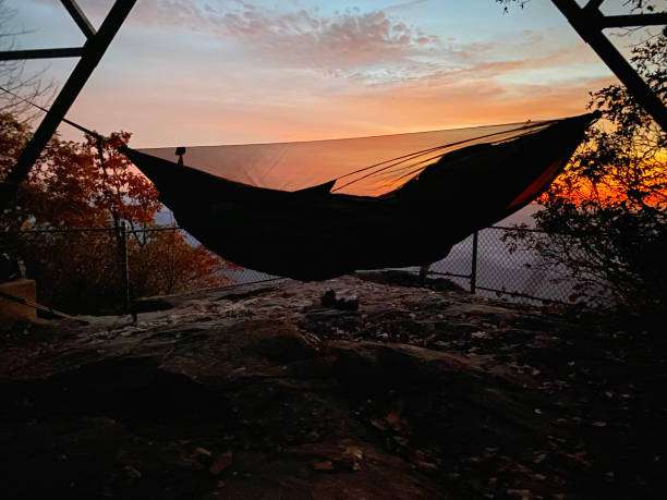 Silhouette of a hammock overlooking a stunning vibrant sunset from a rocky mountain viewpoint.