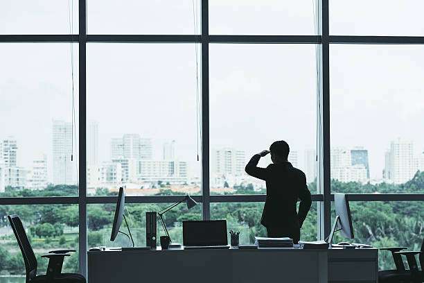 person in office looking out window at city park longing for nature
